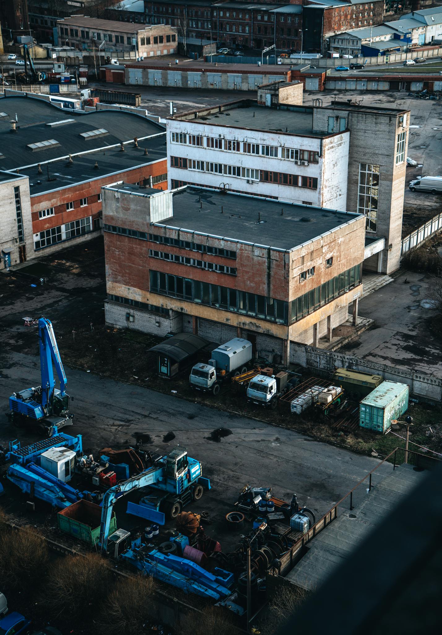 A detailed aerial view of an industrial site with buildings, trucks, and machinery under daylight.
